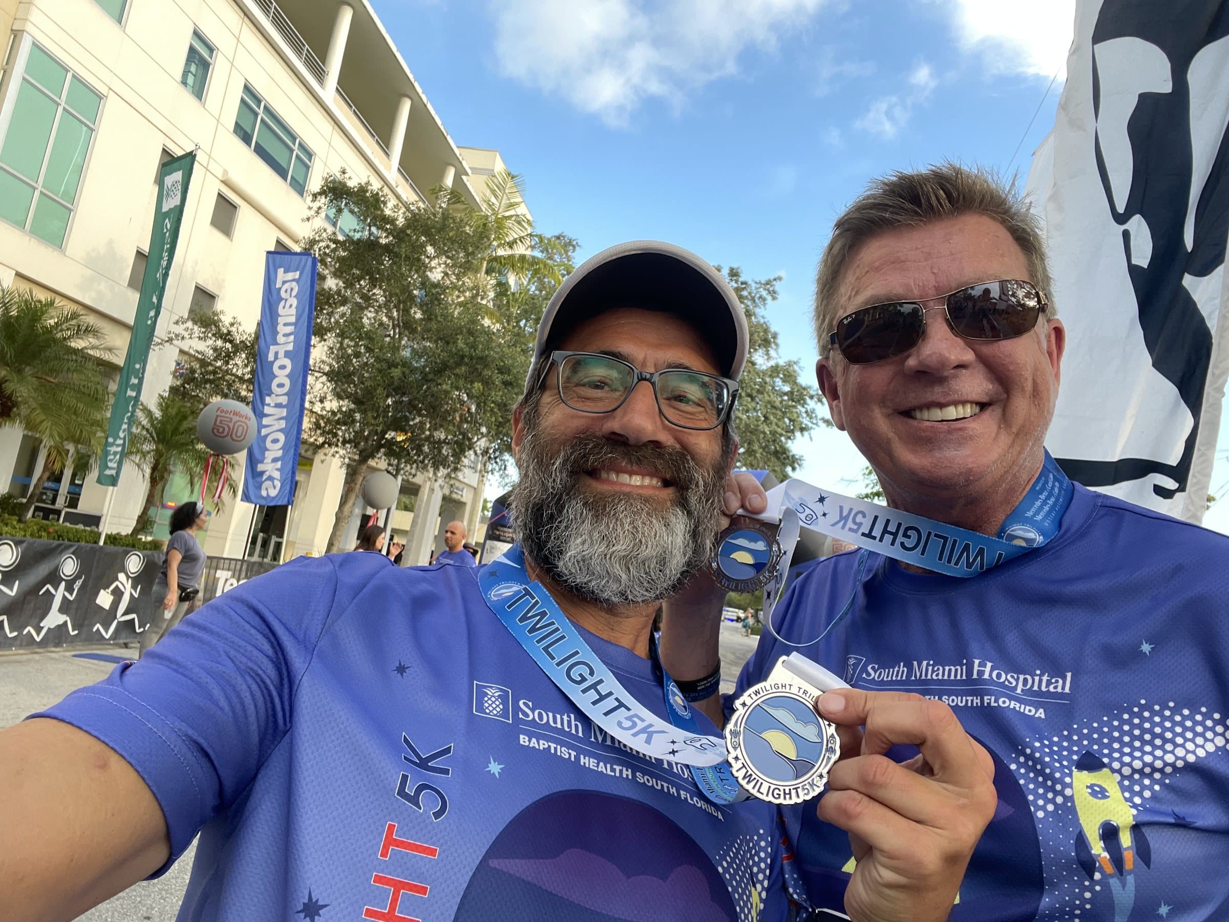 Dwayne and Chaim Backman after a 5K, both wearing finisher medals, Dwayne holding his up to the camera