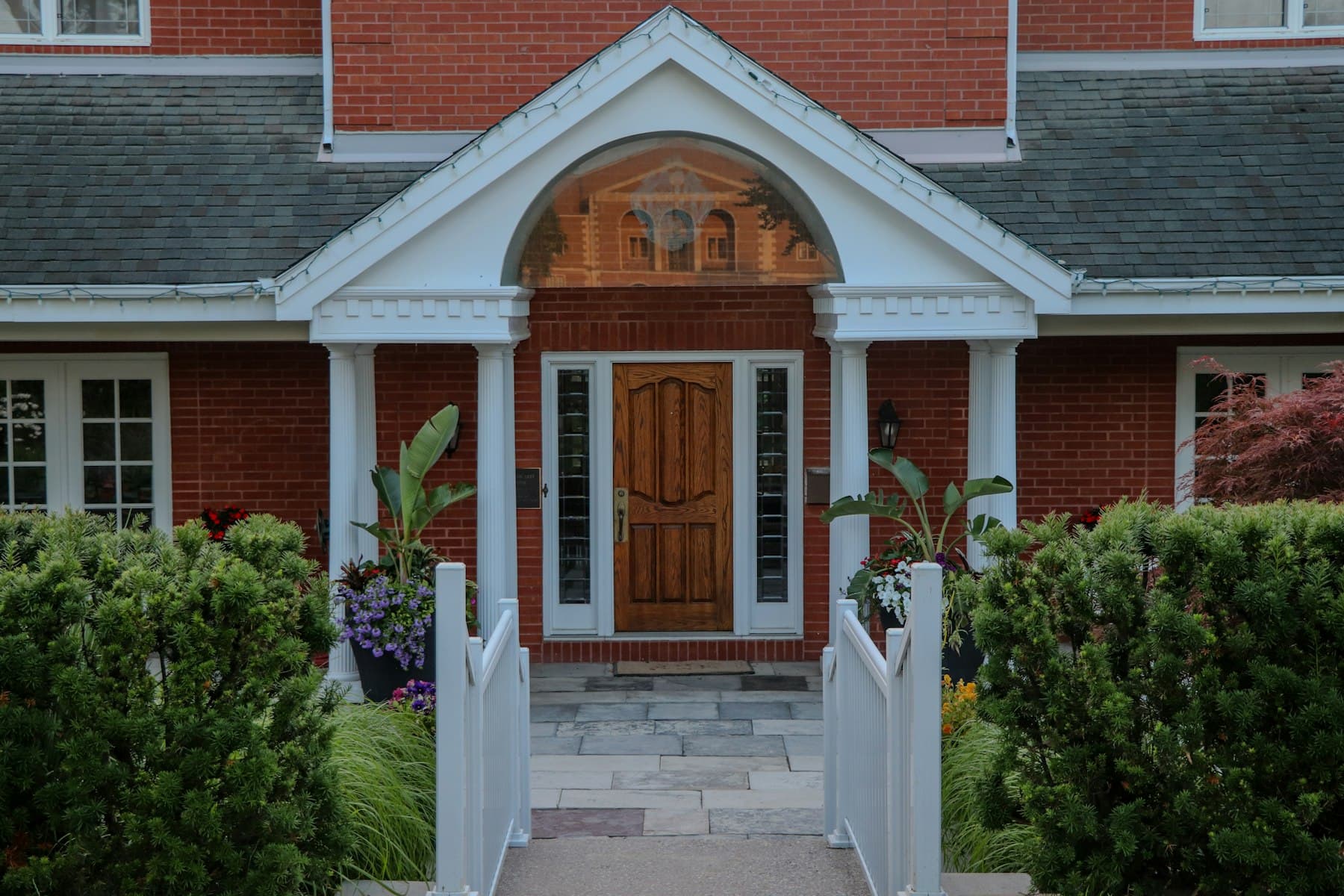 The front entrance of a brick house, columns either side of a wooden door, a path leading in